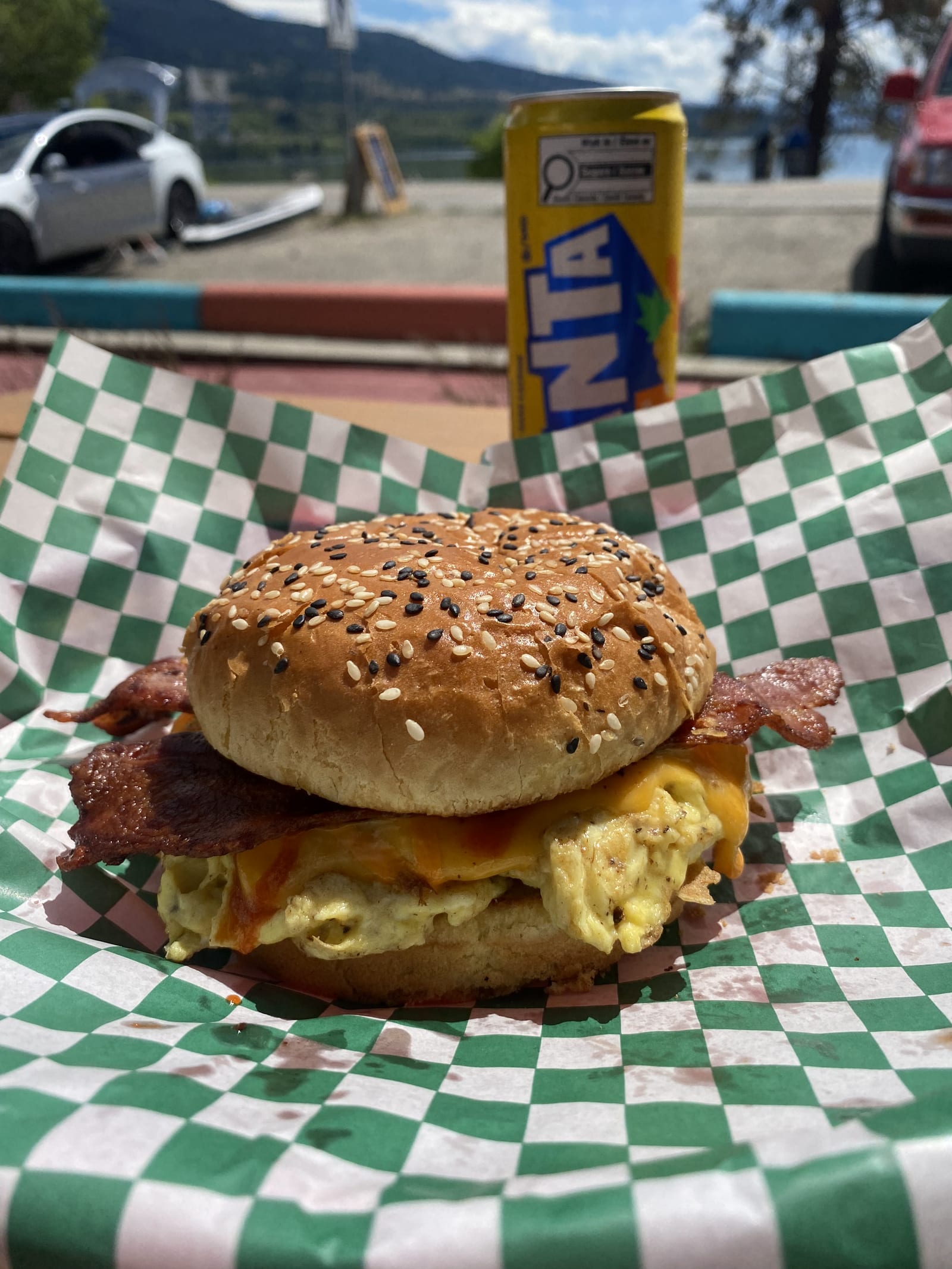 A Lu Lou's breakfast sandwich, egg, bacon and melted cheddar on a toasted sesame bun, in a checker-lined basket on the lakeside deck