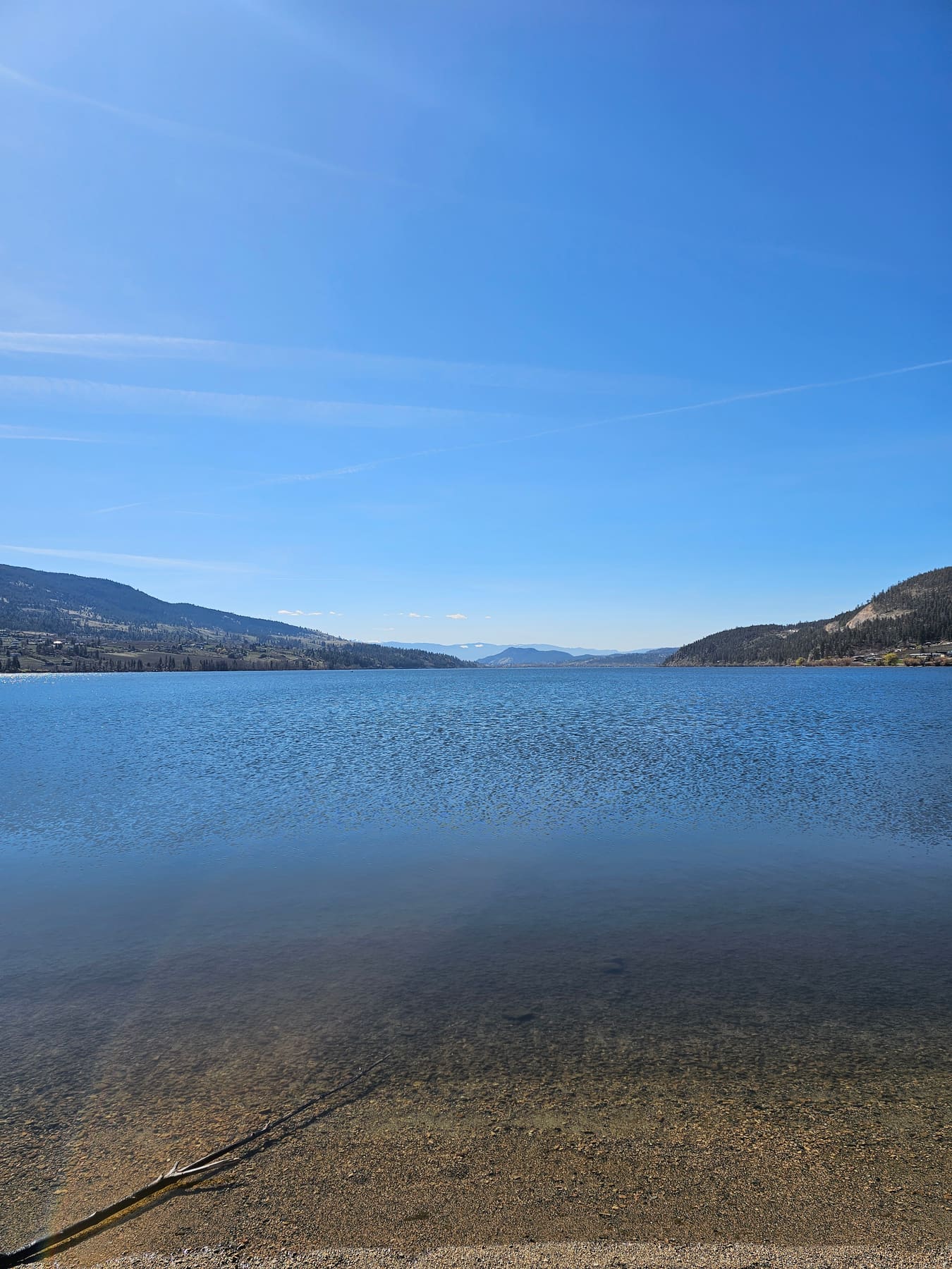 Wood Lake beach in Oyama, BC, looking out across the water to the mountains on a sunny day